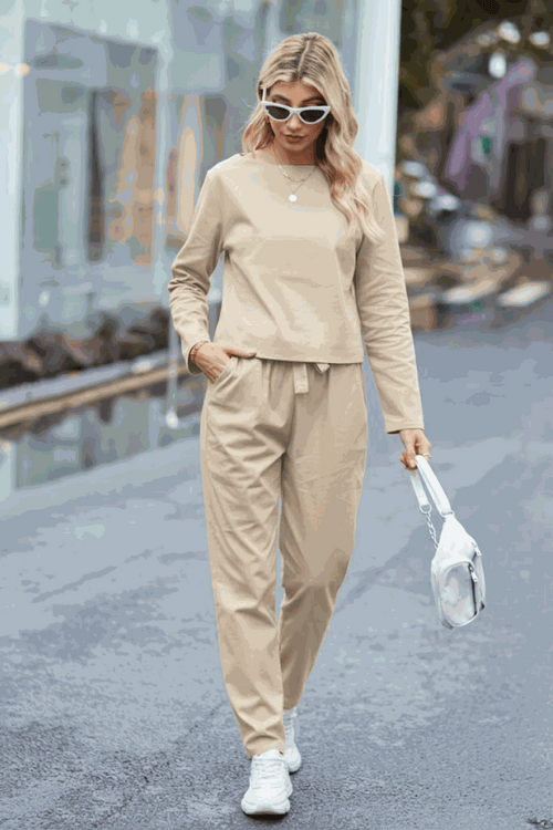Woman wearing beige cotton-linen monochrome relaxed longline top and wide-leg pants set walking outdoors with sunglasses and white sneakers.