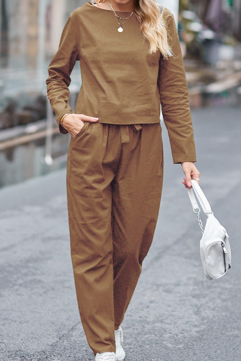 Woman wearing brown 100% cotton linen two-piece set with long sleeves and pants, holding a white handbag.