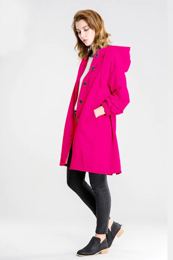 Woman wearing vibrant Barbara Pink Raincoat windbreaker jacket with hood, black pants, and ankle boots against white background