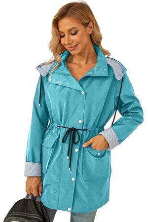 Woman wearing teal water resistant hooded striped windbreaker jacket with drawstring waist and front pockets