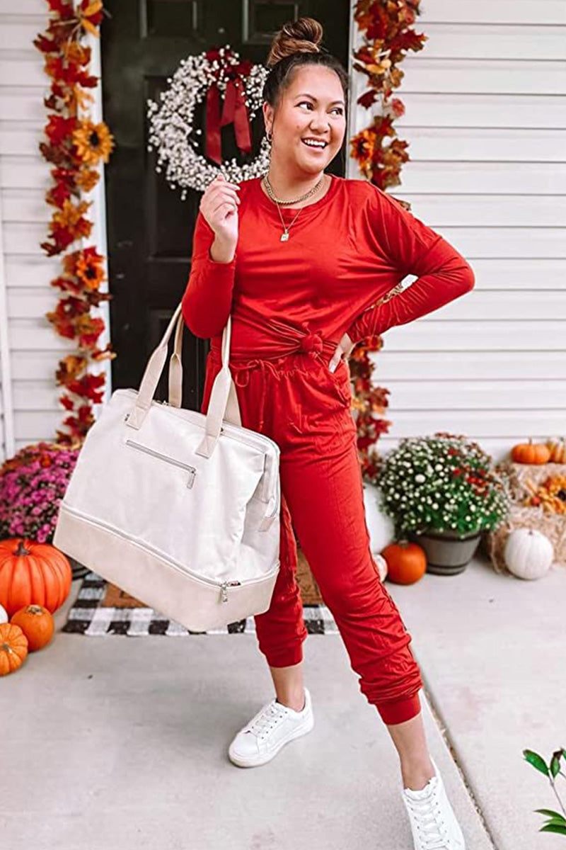 Woman wearing red Cozy Chic Two-Piece Sweatsuit carrying beige tote bag outside decorated house with pumpkins and flowers.