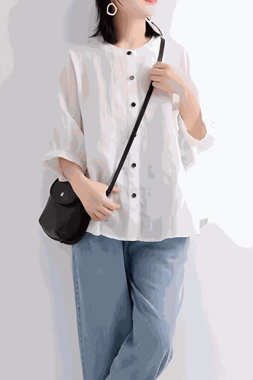 Woman wearing relaxed loose breathable linen blouse in white with rolled sleeves and black buttons paired with light blue jeans and black crossbody bag