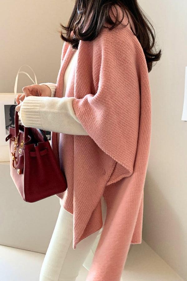 Woman wearing a relaxed flowy open front knitwear cardigan in soft pink with white sleeves holding a red handbag indoors