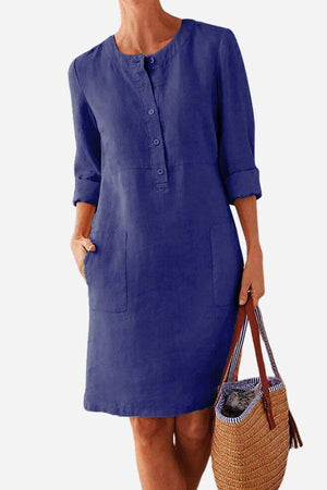 Blue cotton dress with button front, 3/4 rolled sleeves, and pockets, styled with a woven handbag.