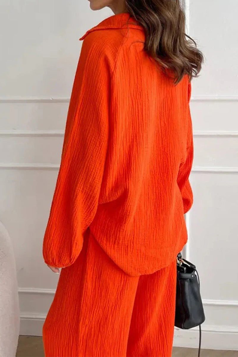 Woman wearing bright orange 100% cotton collared two-piece set with bishop sleeves, back view, holding black handbag.