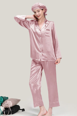 Woman wearing classic pink Mulberry silk pajama set with matching sleep cap, standing on neutral background