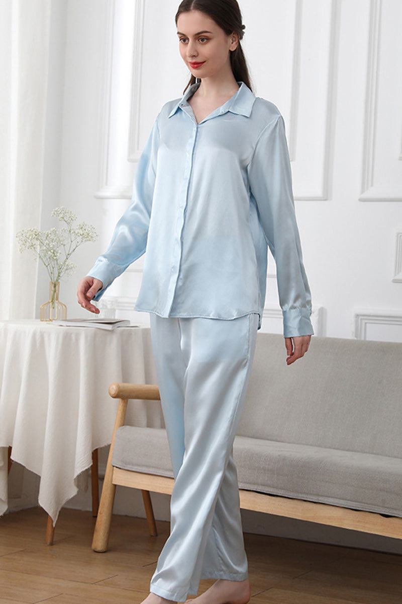 Woman wearing light blue Mulberry silk sleepwear set with long-sleeve button-up top and matching pants in a cozy room.