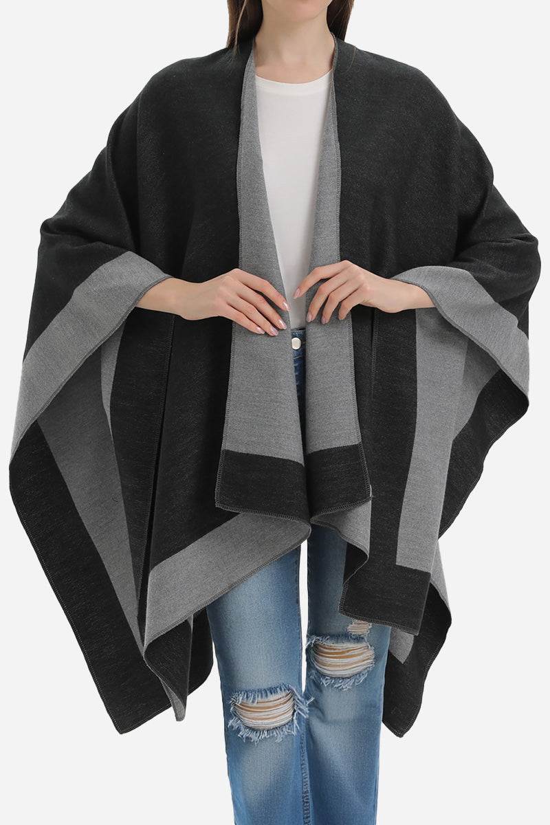 Elegant knitted poncho in two-tone black and gray, draped over casual outfit with jeans, designed for one-size versatility and sophisticated layering.
