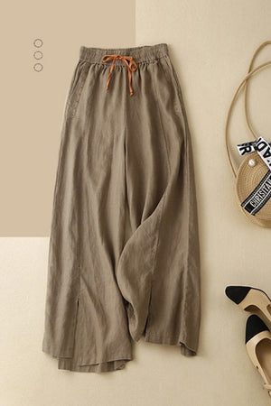 Wide-leg cotton linen Tuscany trousers with elastic waistband and drawstring detail, styled with straw bag and black-tipped shoes on beige background