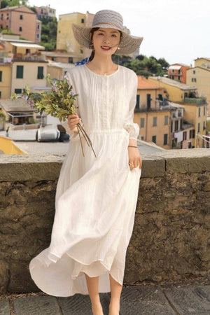 woman wearing white 100% linen coastal shift dress with hat standing outdoors holding flowers