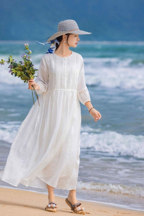 woman wearing white 100 Linen Coastal Shift dress on beach with hat and sandals holding flowers
