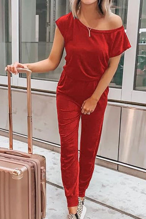 Woman wearing red Moonlit Rome Off-Shoulder Jumpsuit standing next to suitcase in modern urban setting