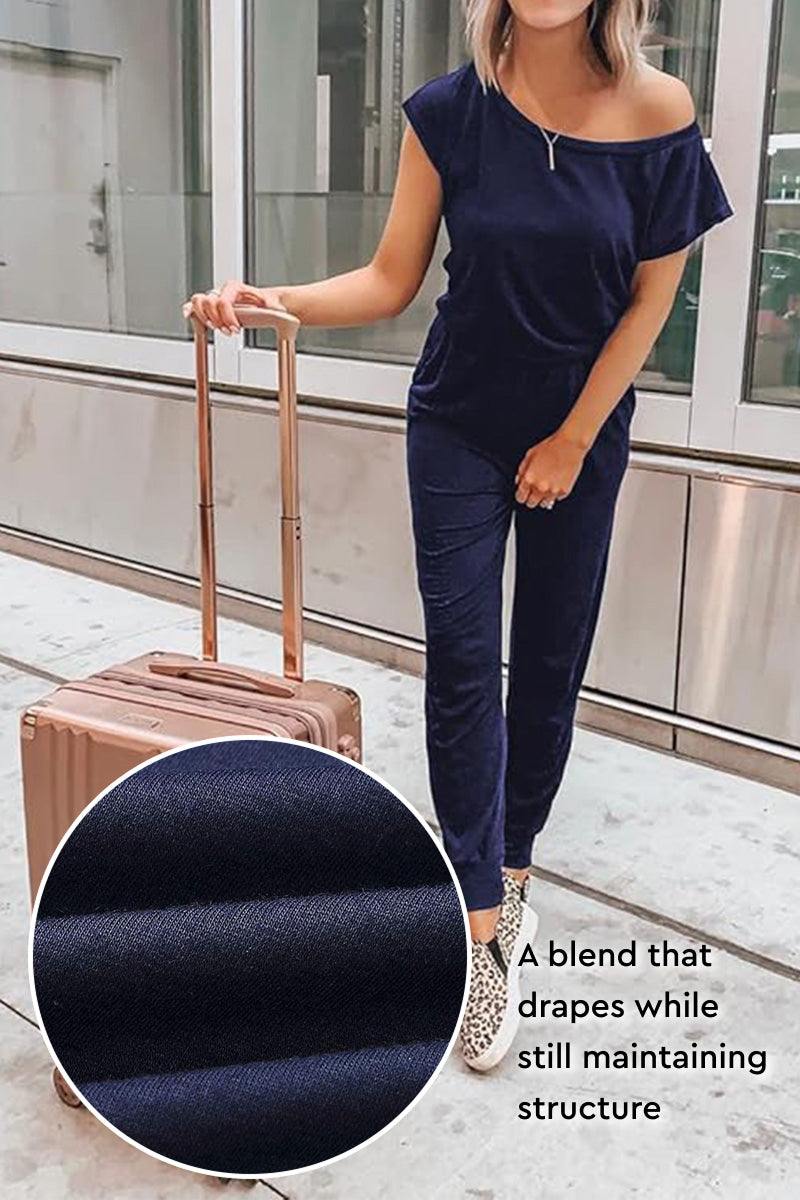 Woman wearing Moonlit Rome Off-Shoulder black jumpsuit with tapered legs and side pockets, holding a suitcase in urban setting