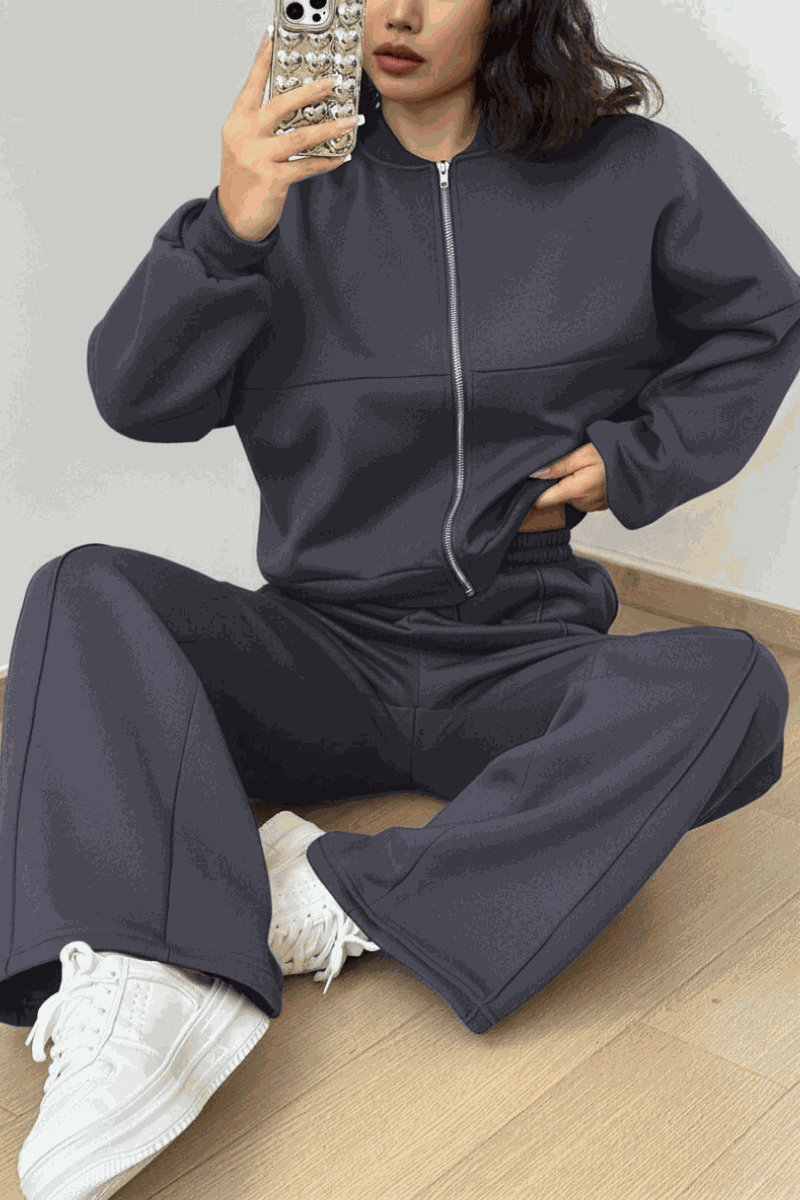 The Voyager Zip Set two-piece zip-front sweatshirt and wide-leg joggers in dark gray with pockets, styled with white sneakers for comfortable travel and casual wear.
