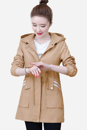 Woman wearing tan Cityscape Comfort Hooded Windbreaker jacket with front pockets and adjustable waist drawstring.