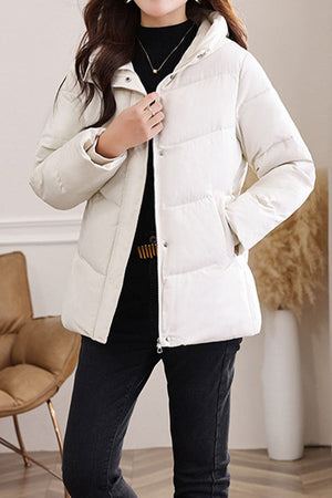 Woman wearing lightweight Everyday Warmth Coat in off-white with mid-length, hooded, relaxed fit and black pants indoors