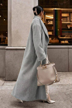 Woman wearing a gray oversized teddy coat with ankle-length coverage and oversized lapels, styled with high heels and a beige handbag