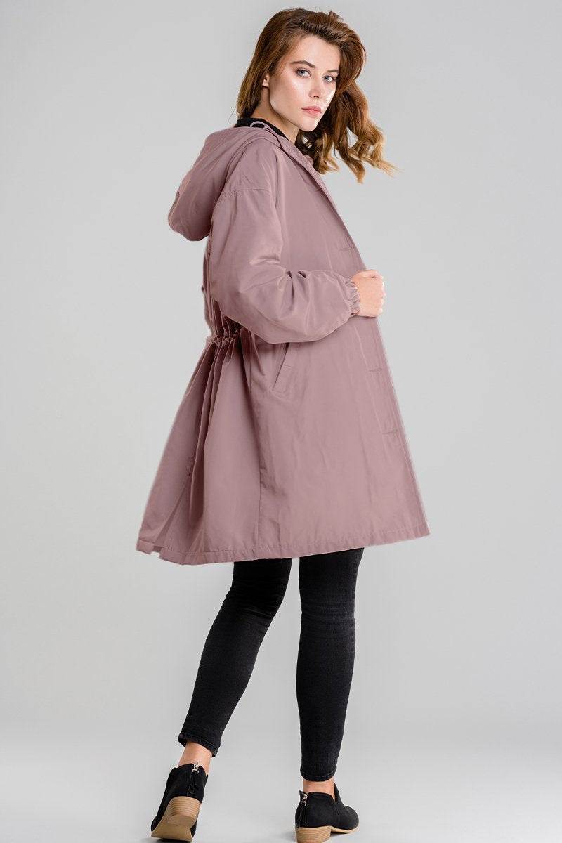 Woman wearing oversized mauve water-resistant windbreaker jacket with hood and black leggings against gray background