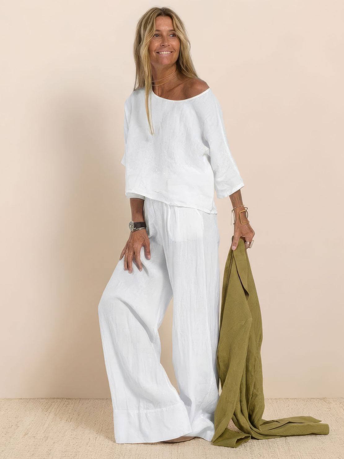 Woman wearing a white short-sleeved pullover and wide trouser matching set holding a green jacket.