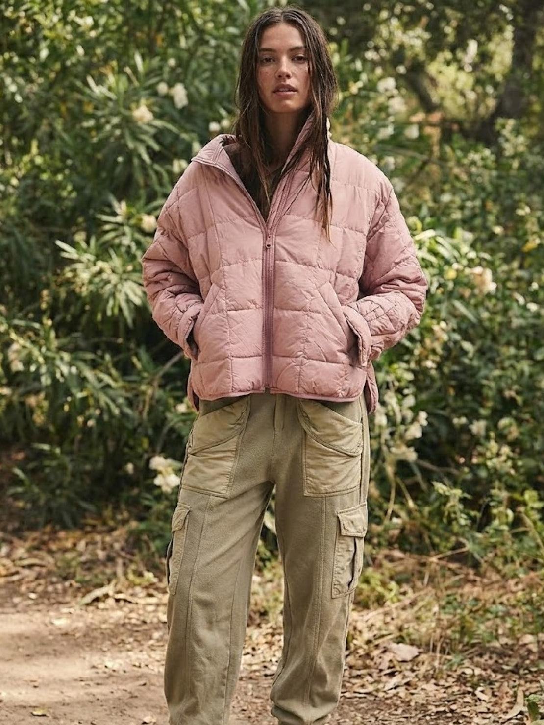 Woman wearing a pink lightweight puffer travel jacket and khaki cargo pants outdoors