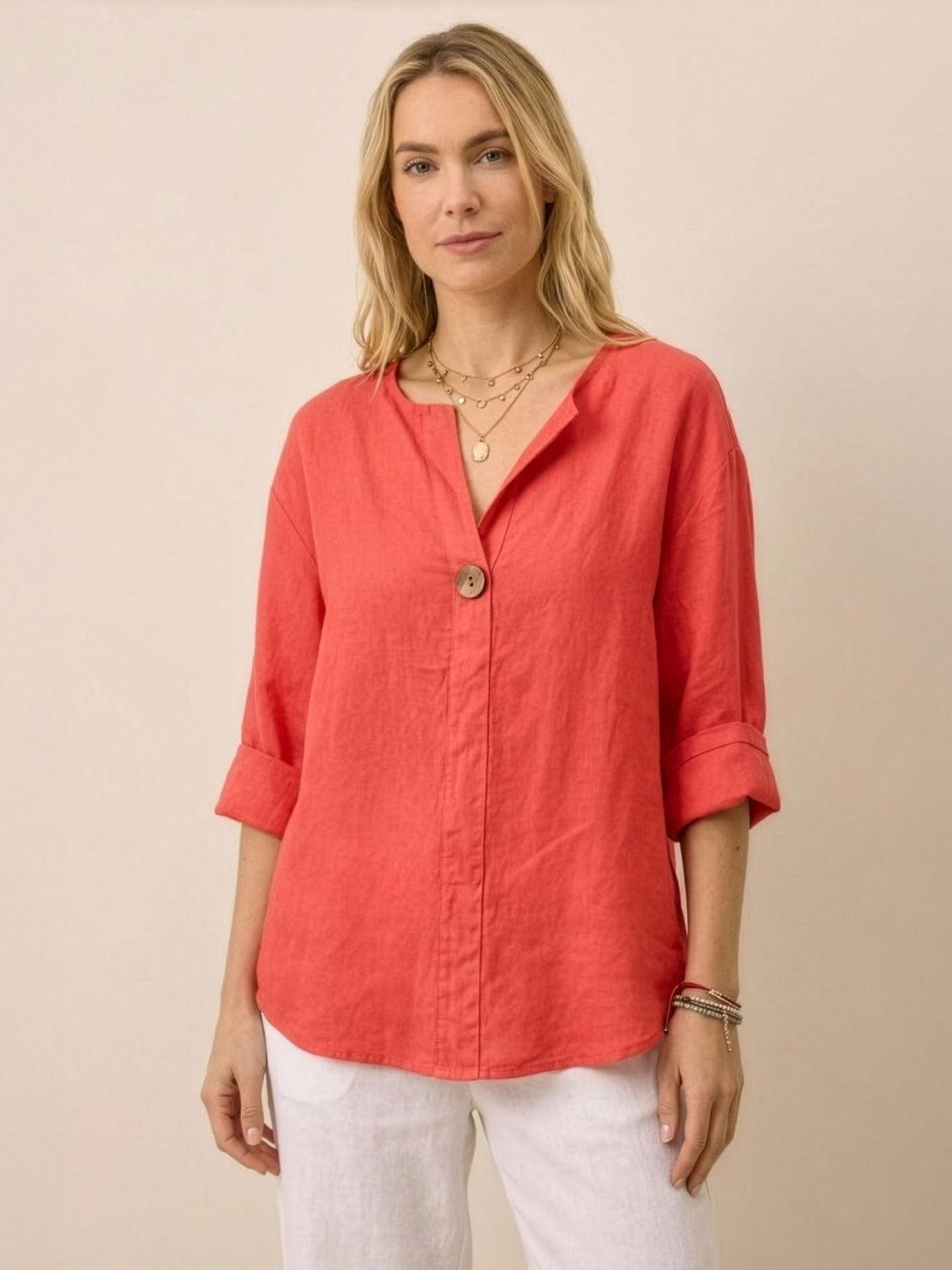 woman wearing coral pure linen age-defying button detail shirt with rolled sleeves and white pants