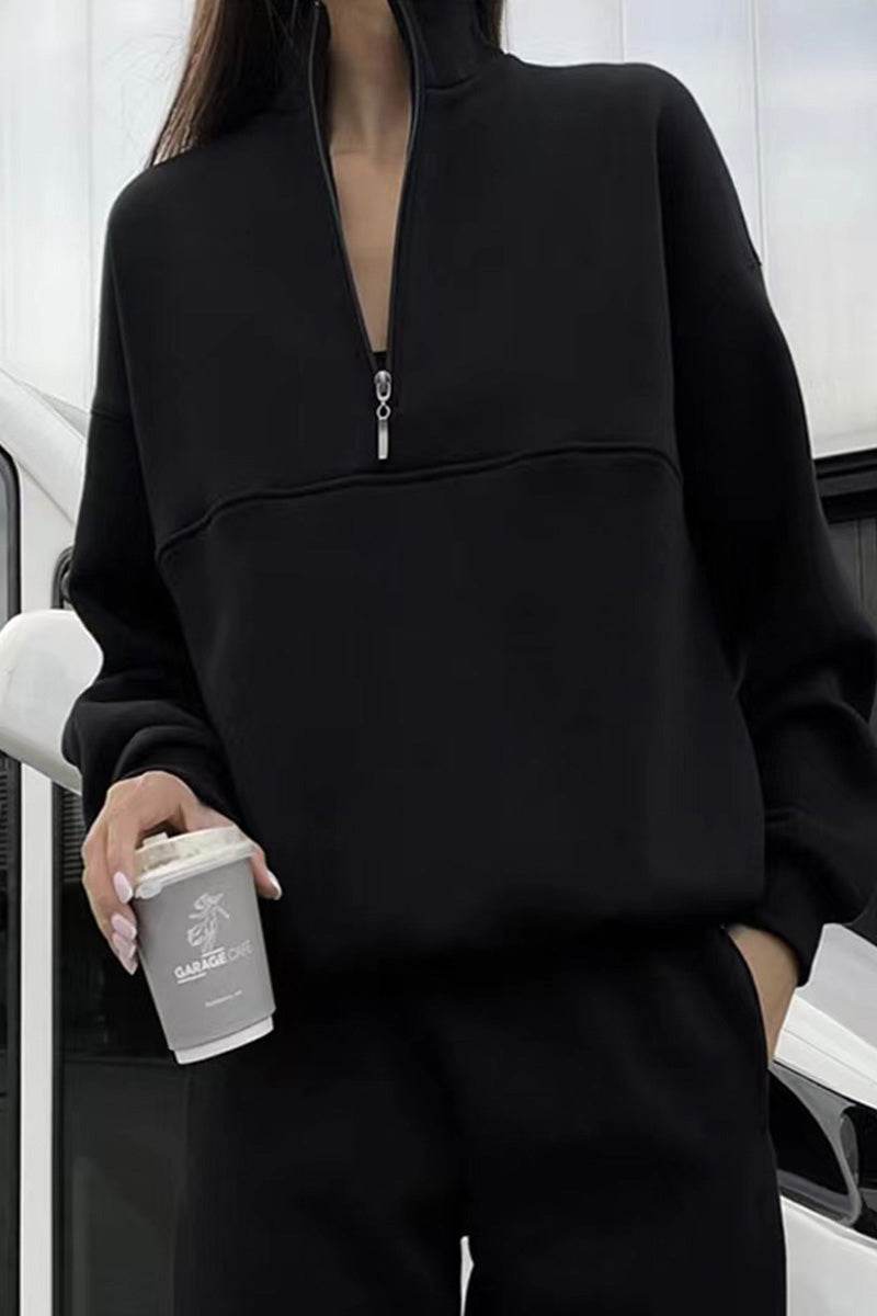 woman wearing black Classic Airplane Set two-piece tracksuit with half-zip pullover and tapered joggers holding a coffee cup