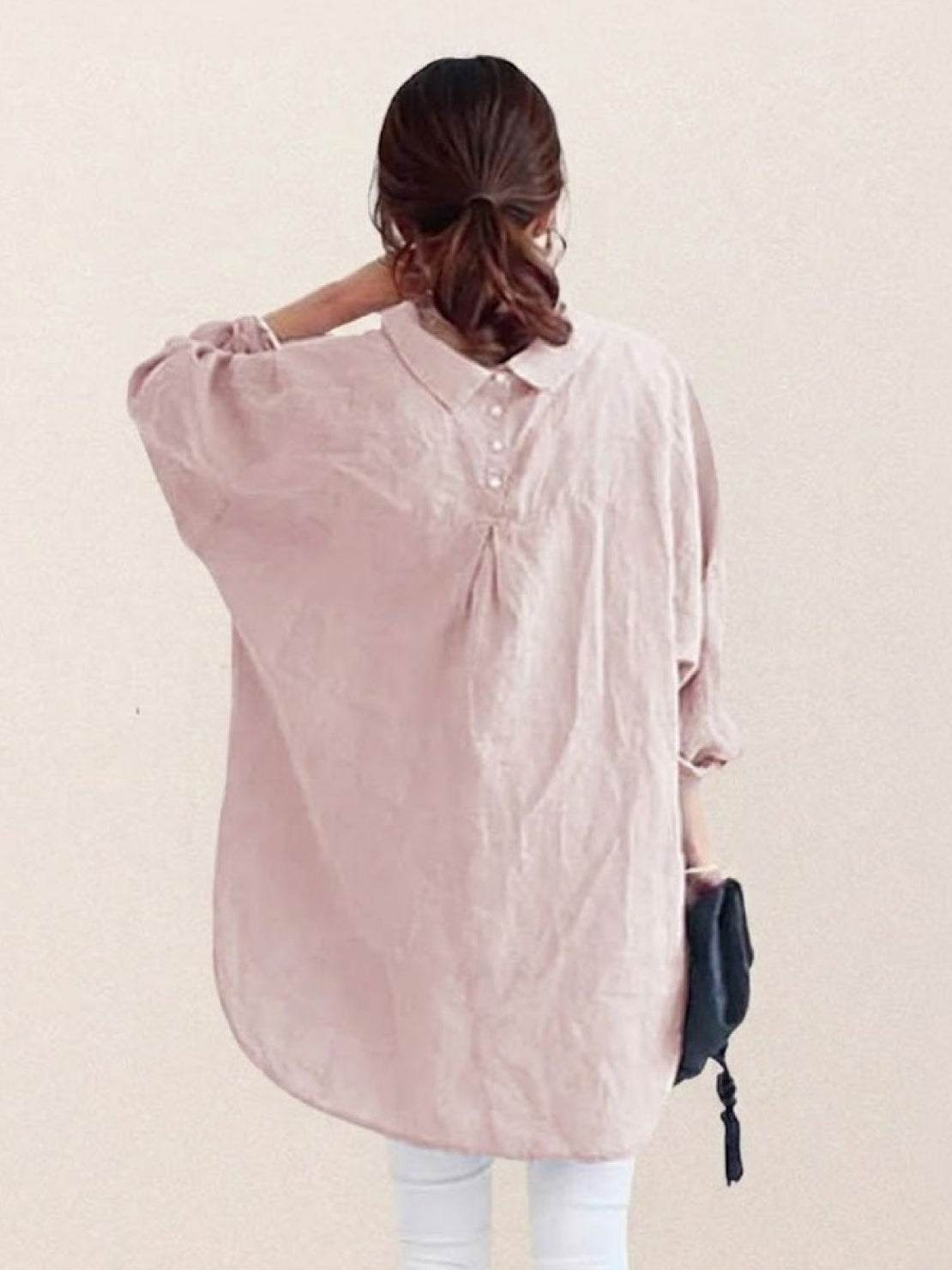 Woman wearing oversized linen shirt with loose sleeves and back button detailing in soft white color