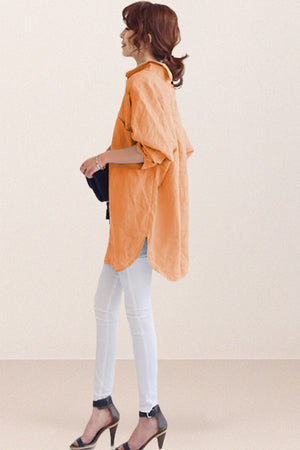 Side view of a woman wearing an oversized linen shirt in soft orange with rolled-up sleeves, paired with white pants and black heels