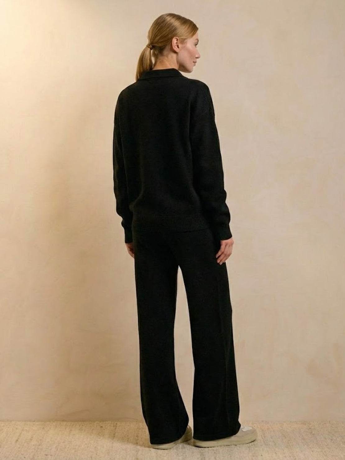 woman wearing black plush and preppy two-piece set with wide-leg pants and long sleeve top standing against beige background