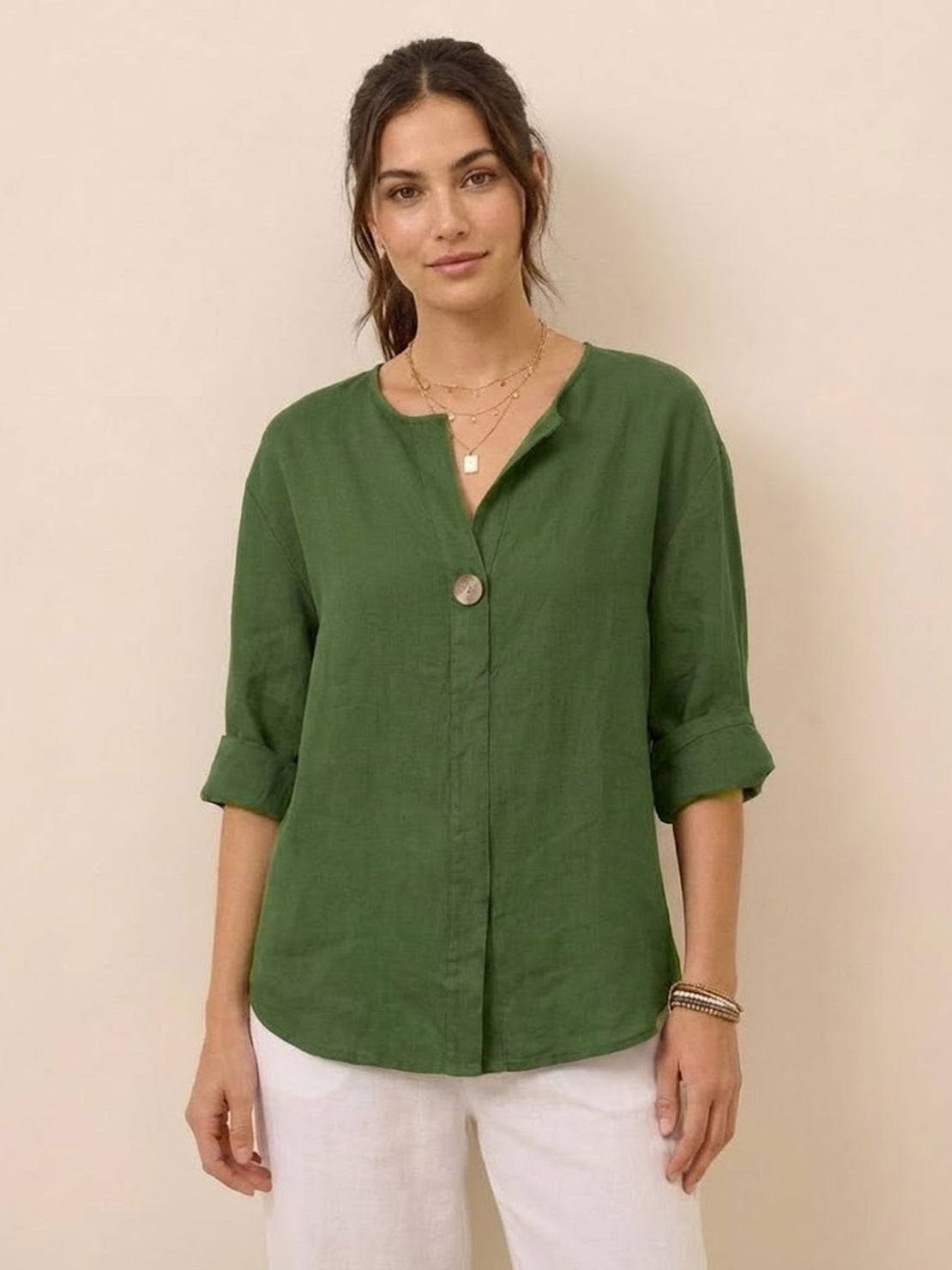 Woman wearing green pure linen age-defying shirt with button detail and rolled sleeves, styled with white pants.