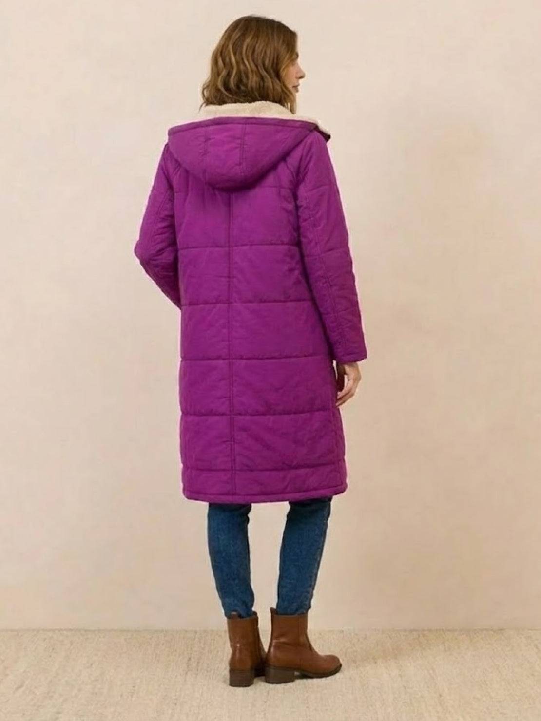 Woman wearing a purple sherpa-lined hooded teddy coat with long silhouette and quilted puffer design, paired with jeans and brown boots.