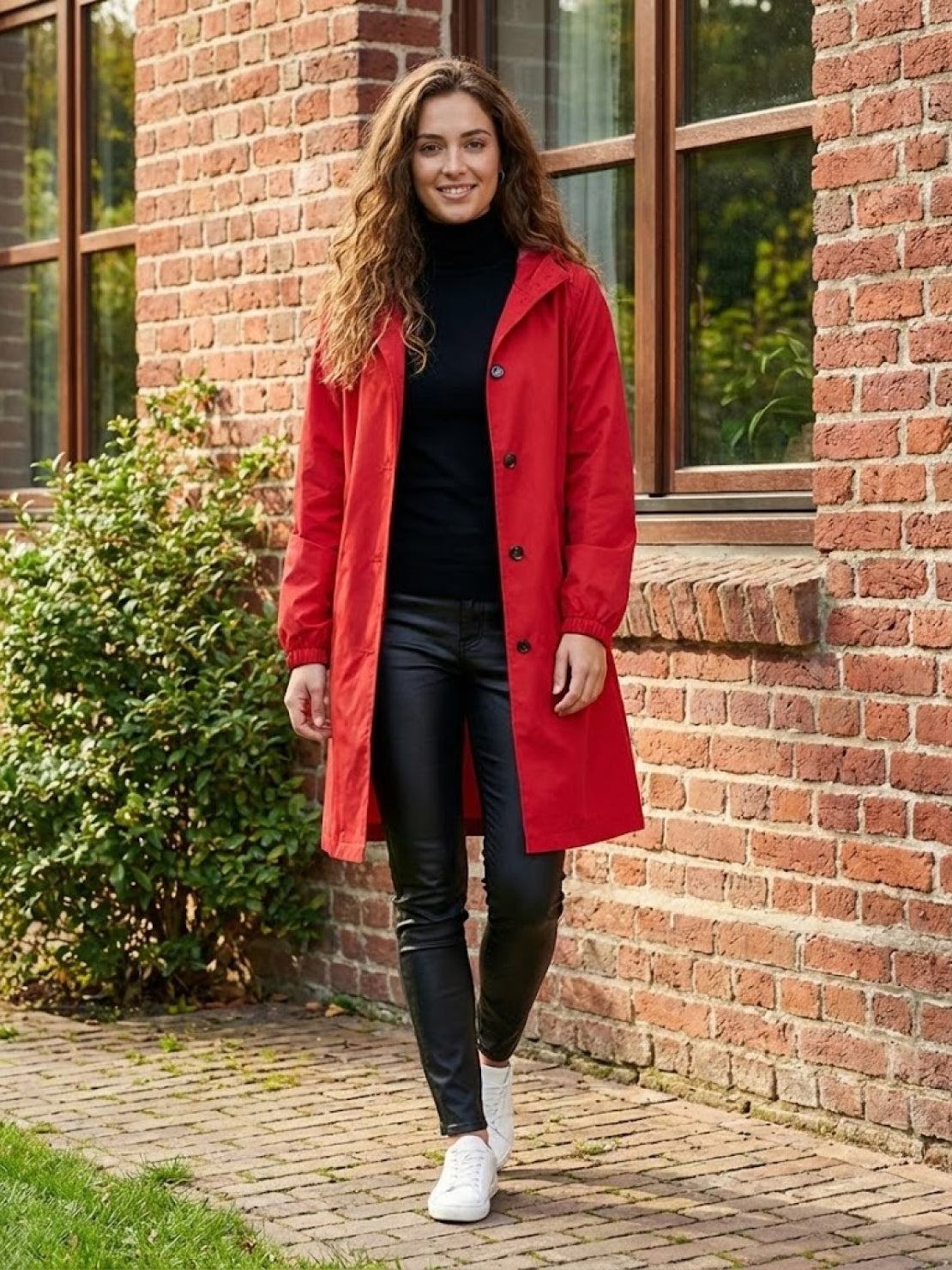 Woman wearing red Rain Couture Windbreaker with black outfit and white sneakers walking outside brick building