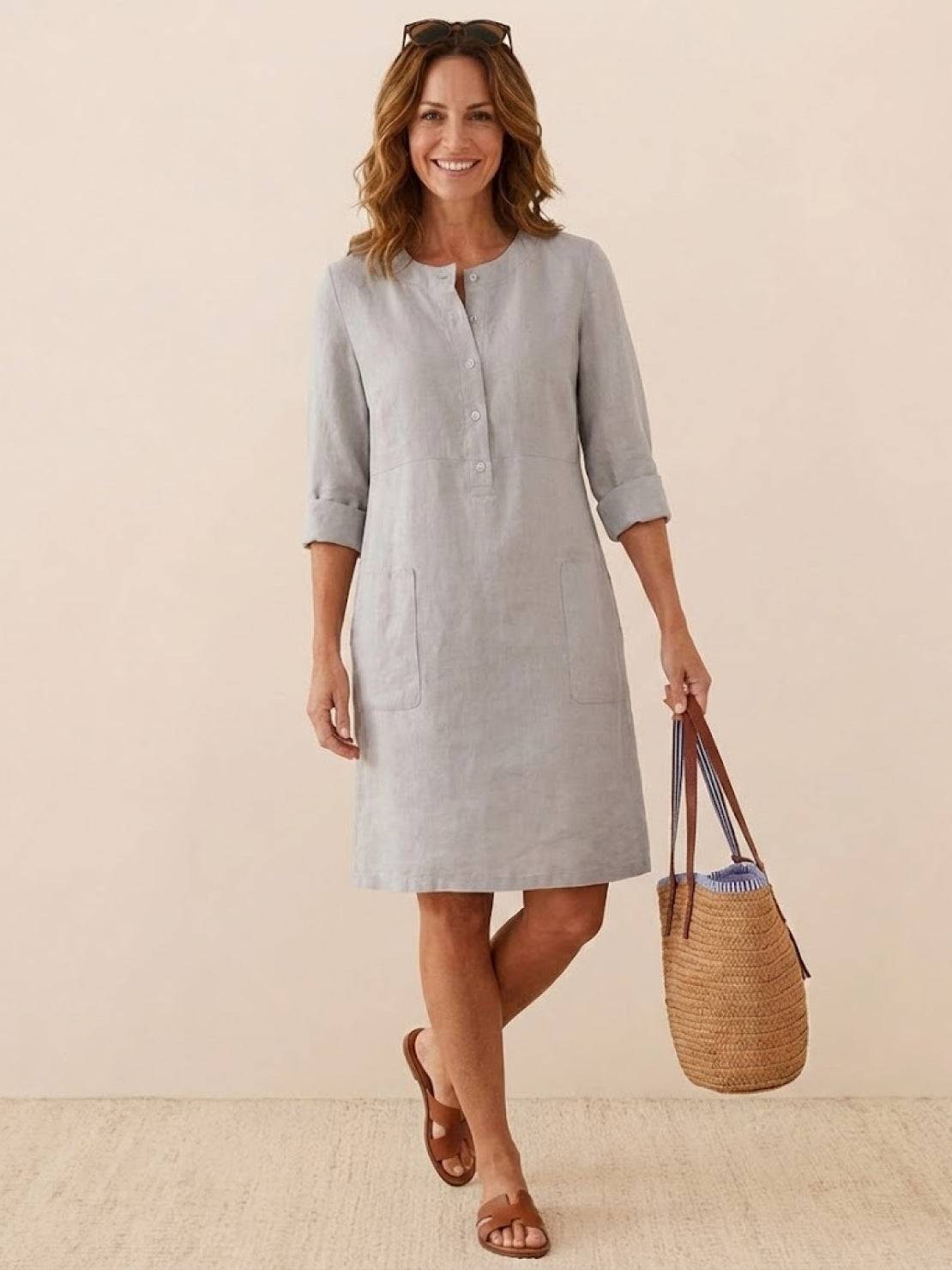 Woman wearing light gray cotton dress with 3/4 rolled sleeves and front pockets carrying straw tote bag