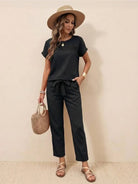 Woman wearing 100% cotton total comfort black two-piece travel set with short sleeves and drawstring pants, accessorized with a straw hat and wicker handbag.
