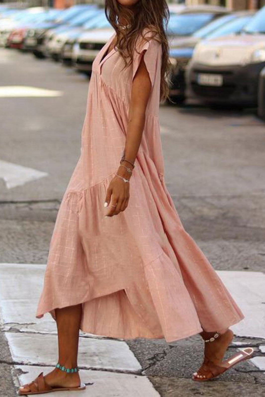 Woman wearing a pink V neck tiered cotton midi dress with short sleeves and frill hem walking outdoors