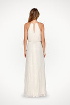 Back view of a woman wearing a white sleeveless belted maxi pleated dress with a keyhole neck detail