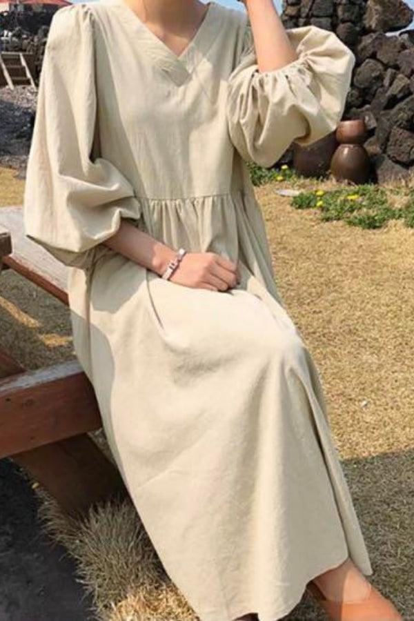 Woman wearing beige midi long sleeve spring dress with V-neck and loose fit sitting outdoors