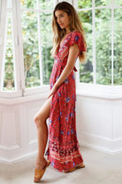 Woman wearing red Bohemian floral print wrap dress with V-neck and high slit indoors by window
