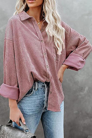 Woman wearing a mauve sleek suede oversized button-down shirt with rolled sleeves and blue jeans holding a gray handbag