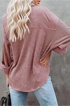 Back view of a woman wearing a sleek suede oversized button-down shirt in dusty rose paired with light blue jeans