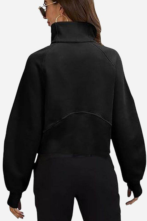 Back view of a woman wearing a black cozy oversized half-zip fleece pullover sweatshirt with long sleeves and a high collar.
