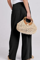 Black oversized palazzo pants paired with a white top and woven handbag in a casual stylish outfit