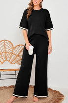 Woman wearing a black short sleeved relaxed fit lounge two-piece set with wide-leg pants and white trim on sleeves and hem, holding a cup.