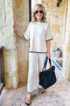 Woman wearing short sleeved relaxed fit lounge two-piece set with wide-leg pants and black trim, holding black handbag.