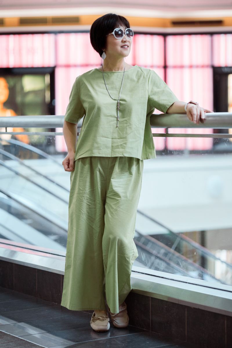 Woman wearing light green loose fit co-ord set with wide-leg pants and short-sleeve top, accessorized with sunglasses and necklace.