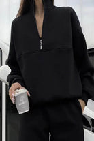 Black cotton-blended two-piece tracksuit with high collar and zipper detail worn by woman holding coffee cup