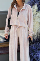 Woman wearing a soft pink zip up cropped sweatshirt and wide leg velour pants leisure two-piece co-ord set.