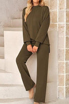 Woman wearing olive green high neck sweater and wide leg pants set standing against beige wall