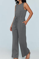 Woman wearing gray sleeveless wide leg pants jumpsuit with drawstring waist and pockets