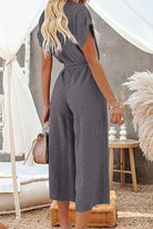 Back view of woman wearing grey V-neck lace-up pocket jumpsuit with tie belt and wide legs